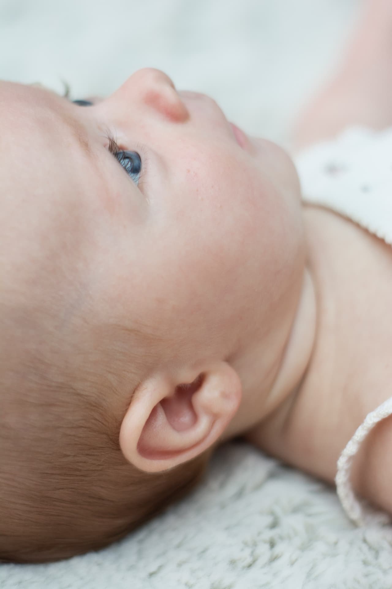 Close-up portrait of a newborn baby's profile showing a bright blue eye and fine hair
