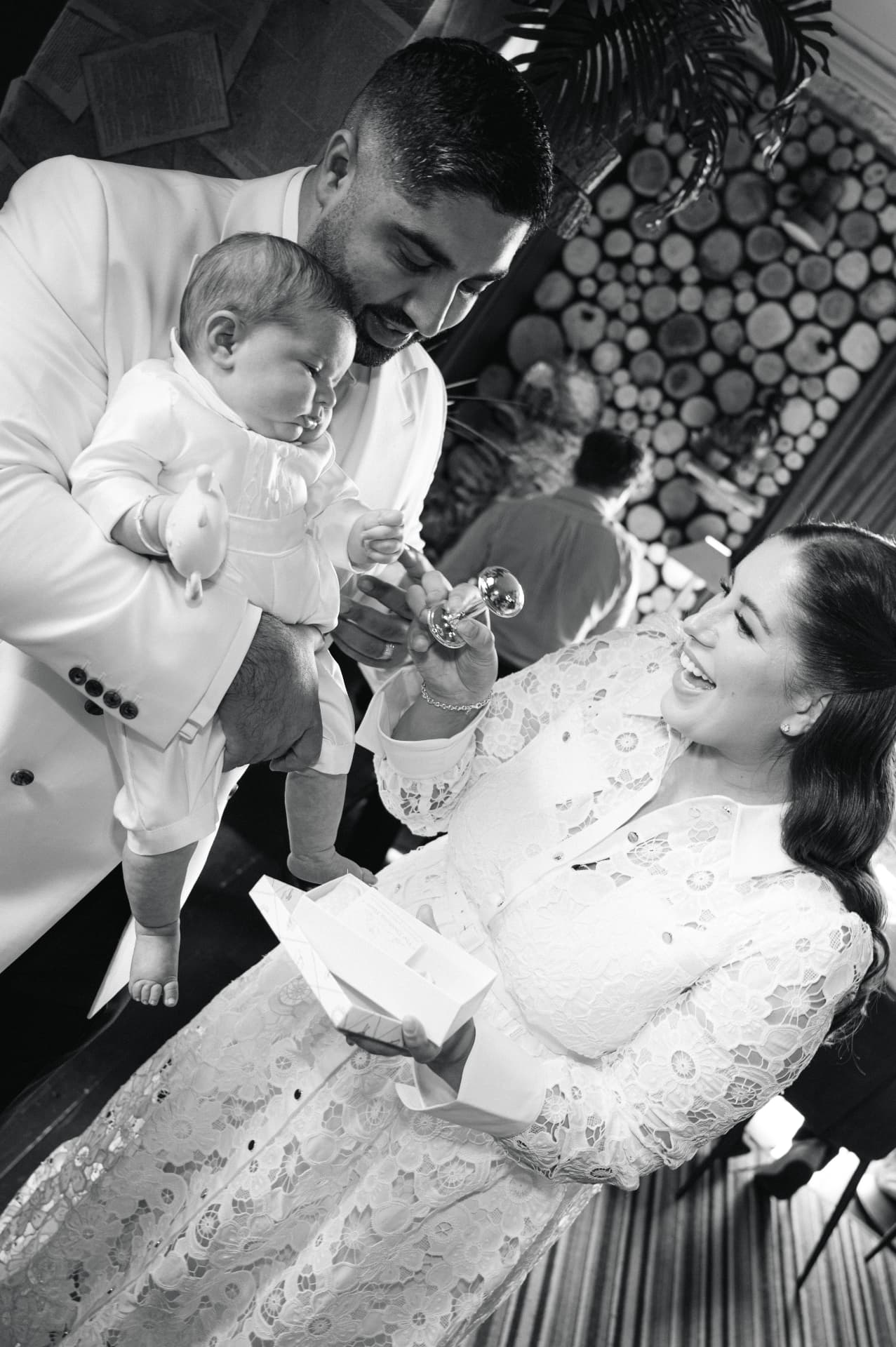 Black and white photograph of parents laughing with their baby at a christening