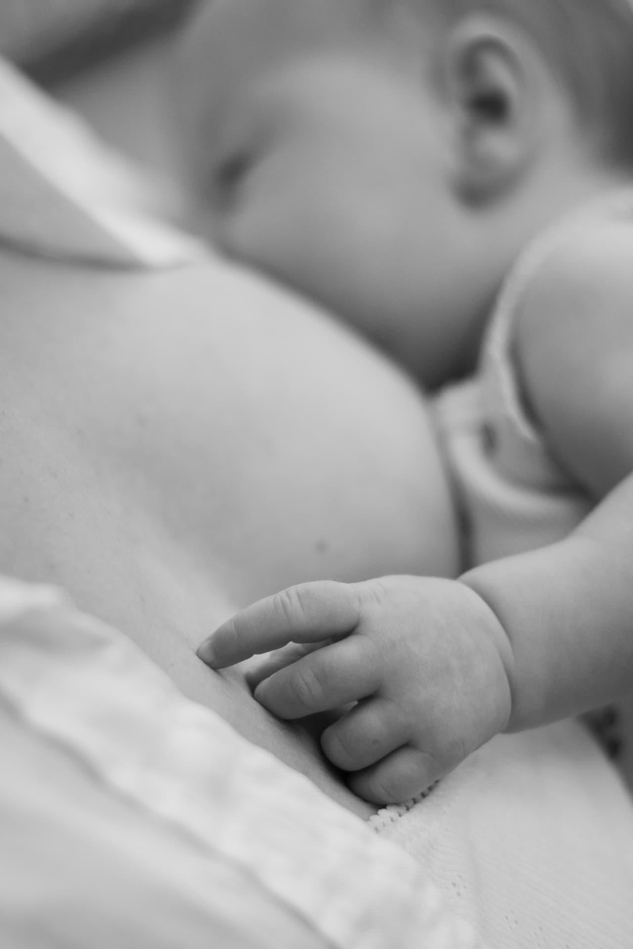 Black and white close-up of a baby's hand resting on a mother's chest