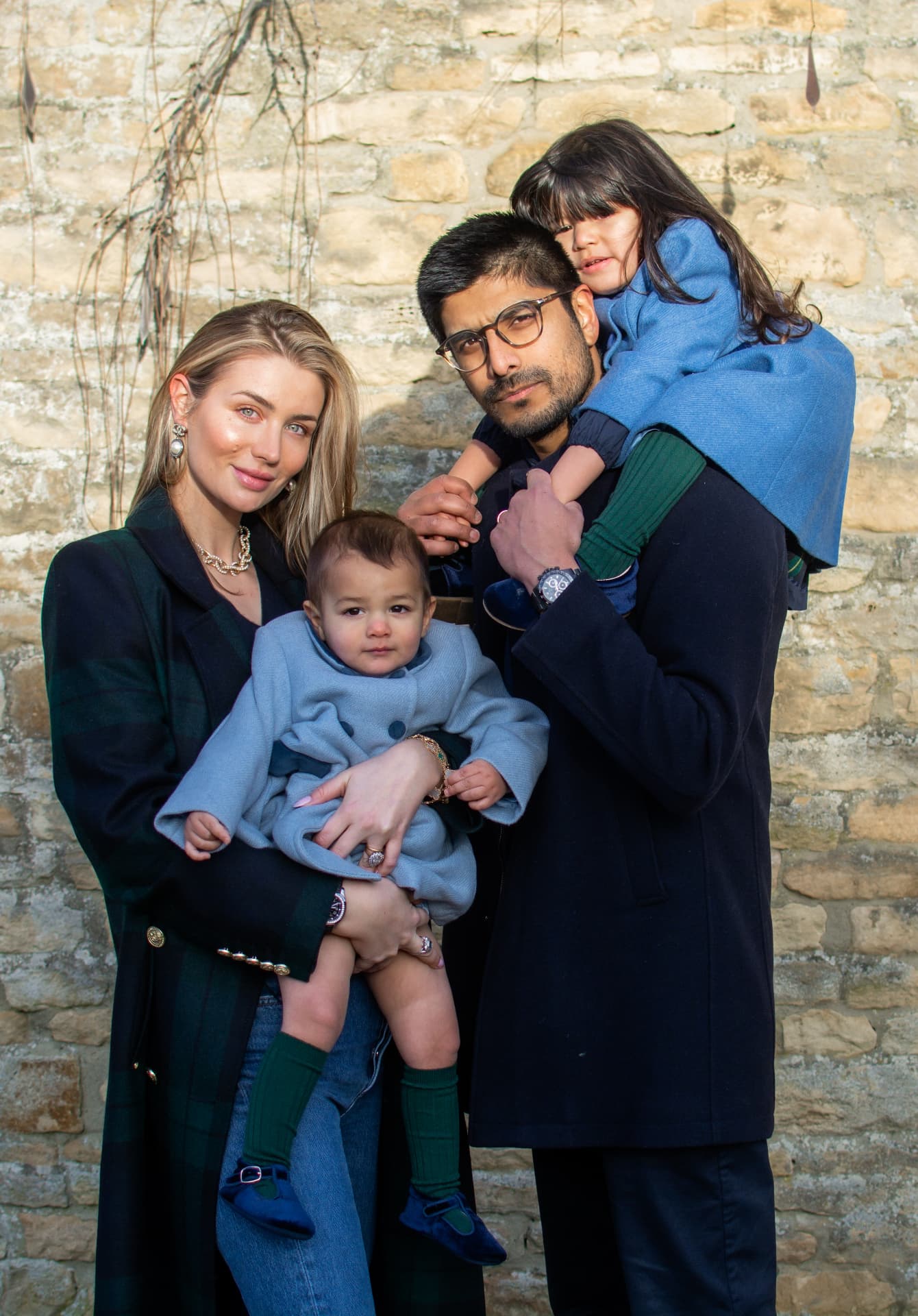 Family of four against a stone wall with a father carrying a girl on his shoulders