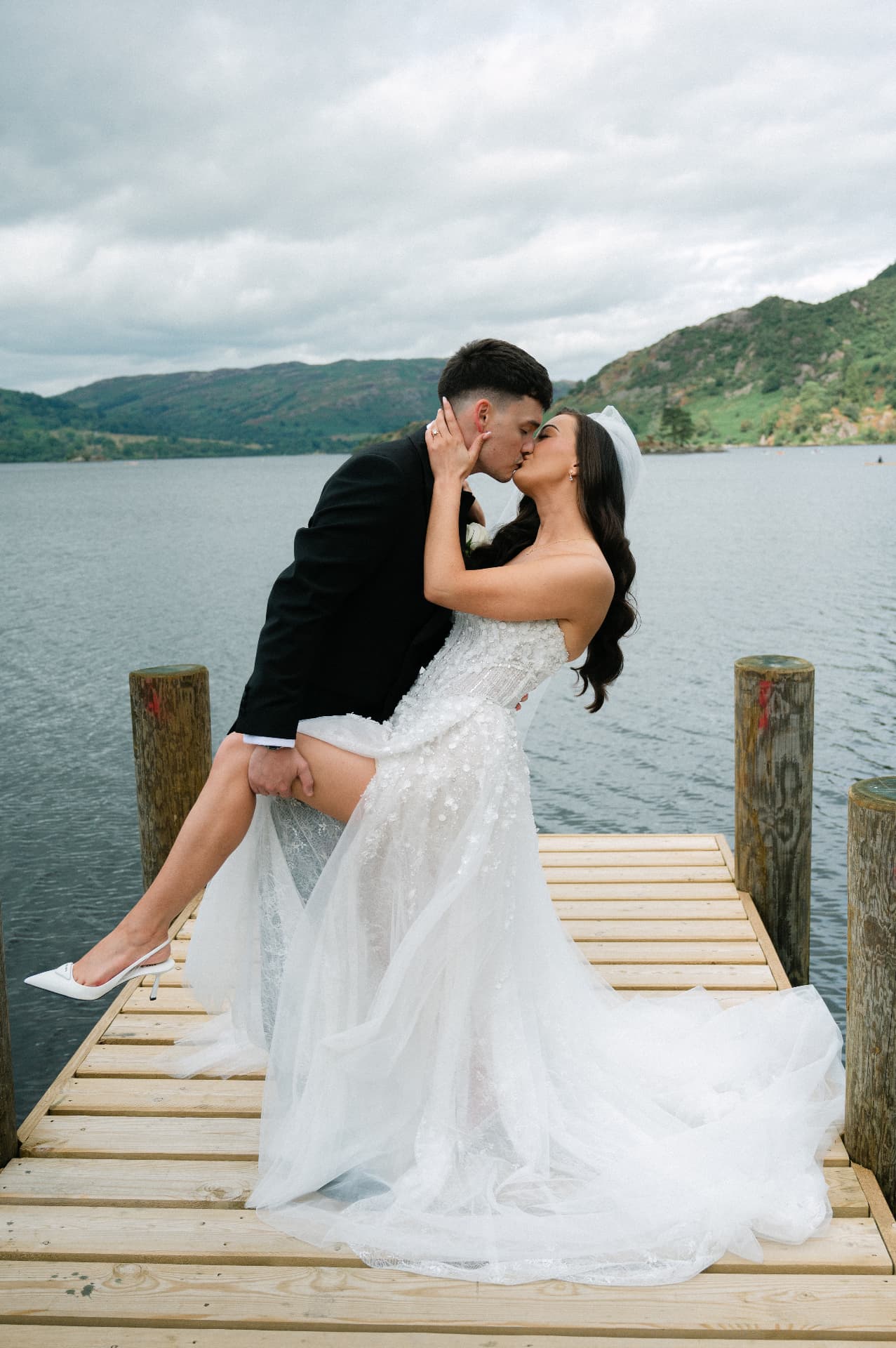 Bride and groom sharing a kiss on a wooden pier over a Lake District lake