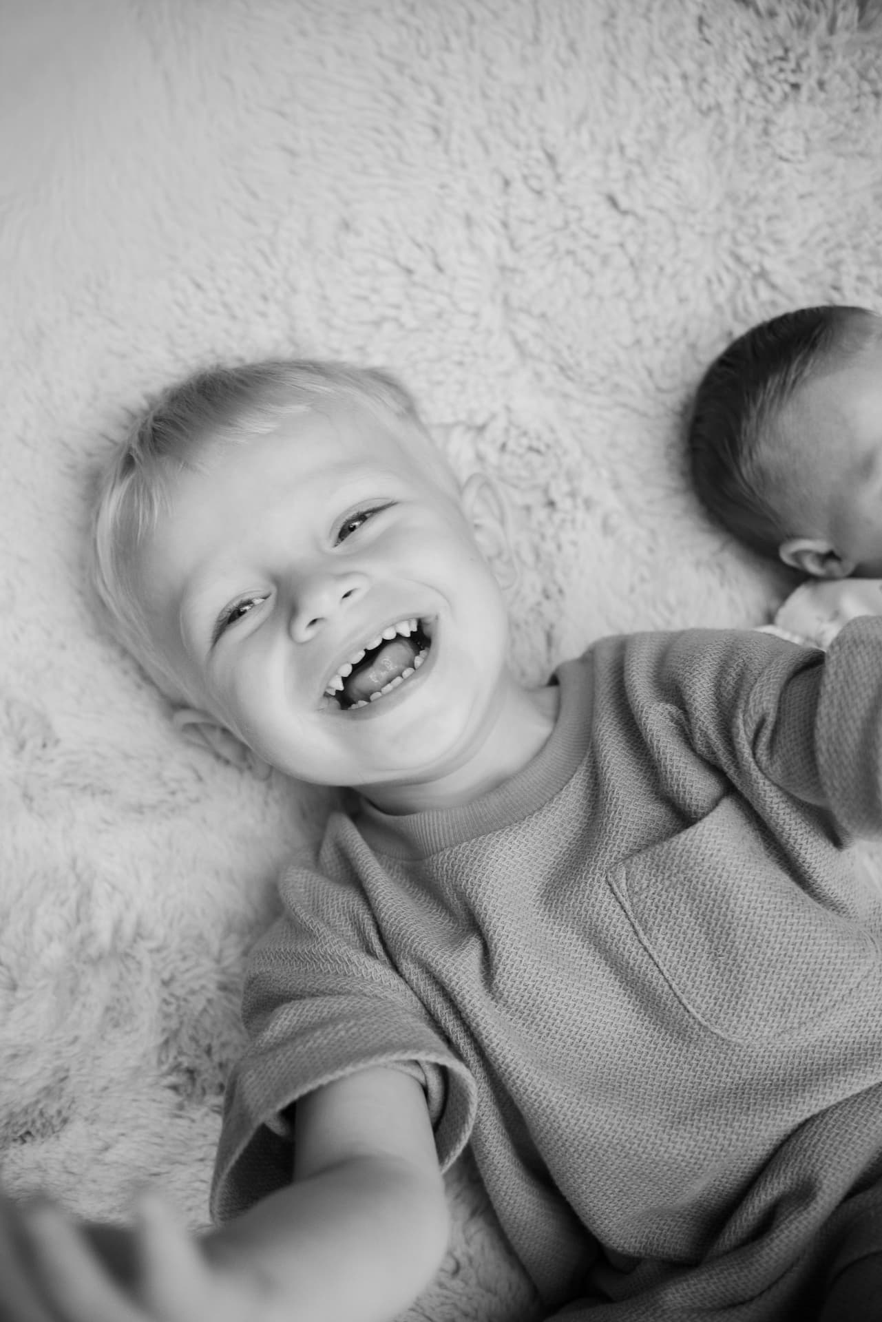 Black and white portrait of a young boy lying on a rug laughing joyfully