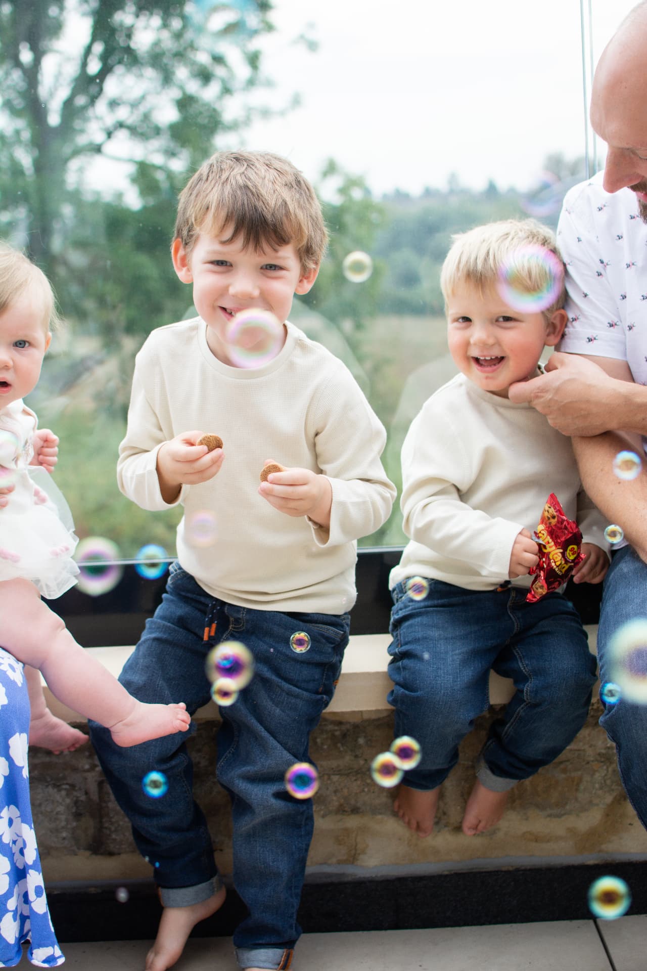 Two young boys sitting on a stone ledge eating cookies with bubbles floating around them