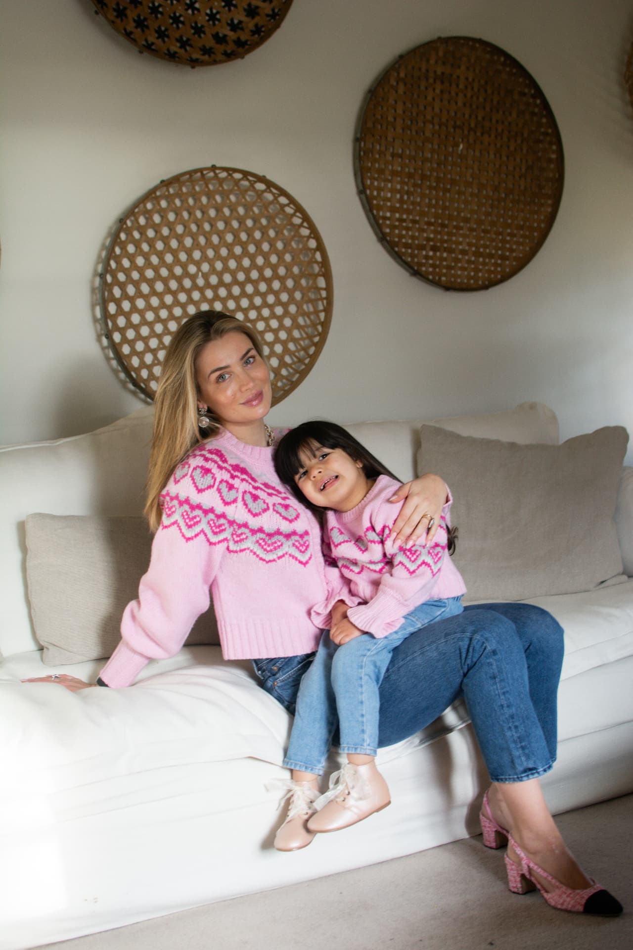 Mother and daughter in matching pink heart sweaters sitting together on a white sofa