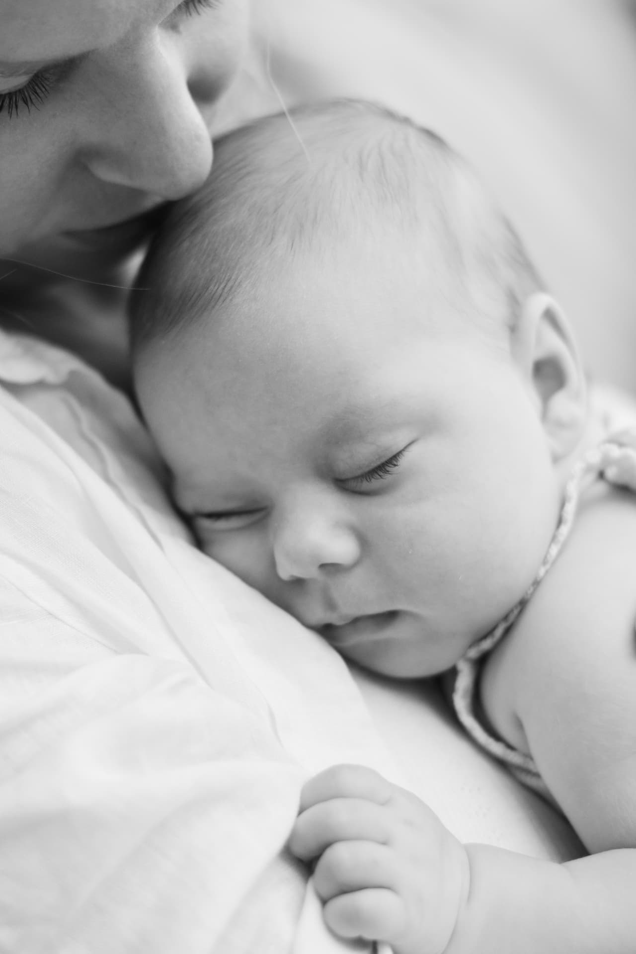 Black and white photograph of a sleeping baby held against their mother