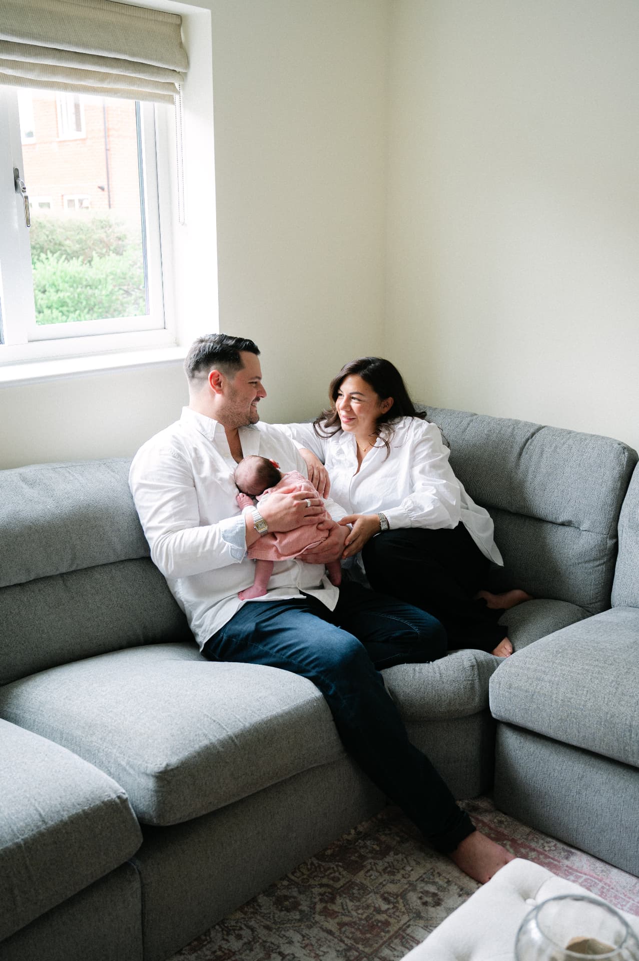 Parents sitting together on a sofa holding their newborn baby