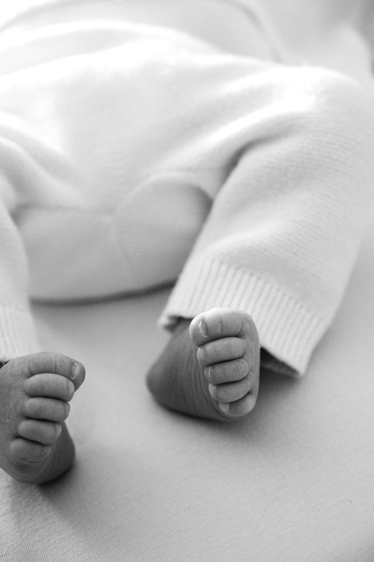 Black and white close-up of a baby's feet in white knitted leggings