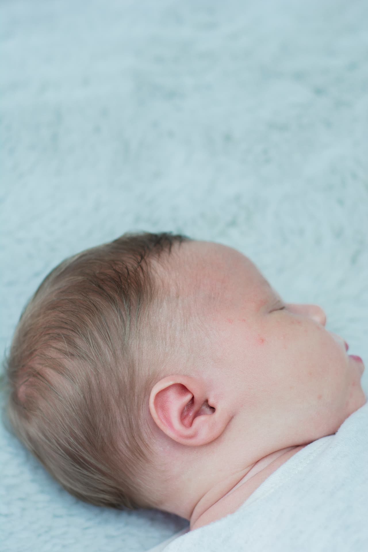 Soft-focus profile of a sleeping newborn against a cool-toned textured background