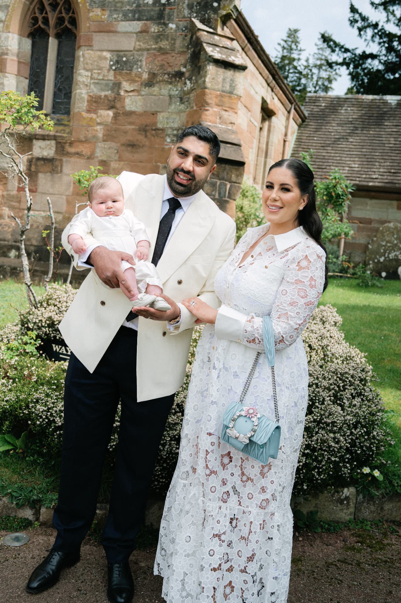 Parents holding their baby outside a stone church on christening day