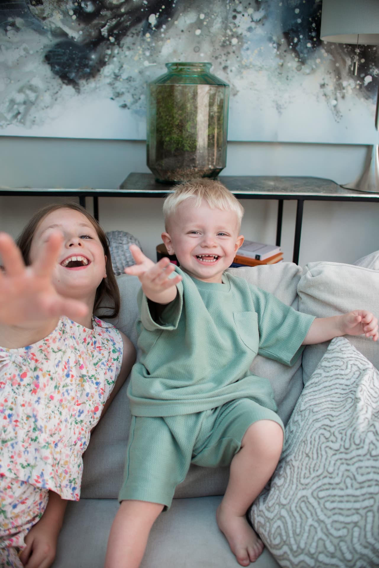Two children laughing and reaching their hands toward the camera on the sofa