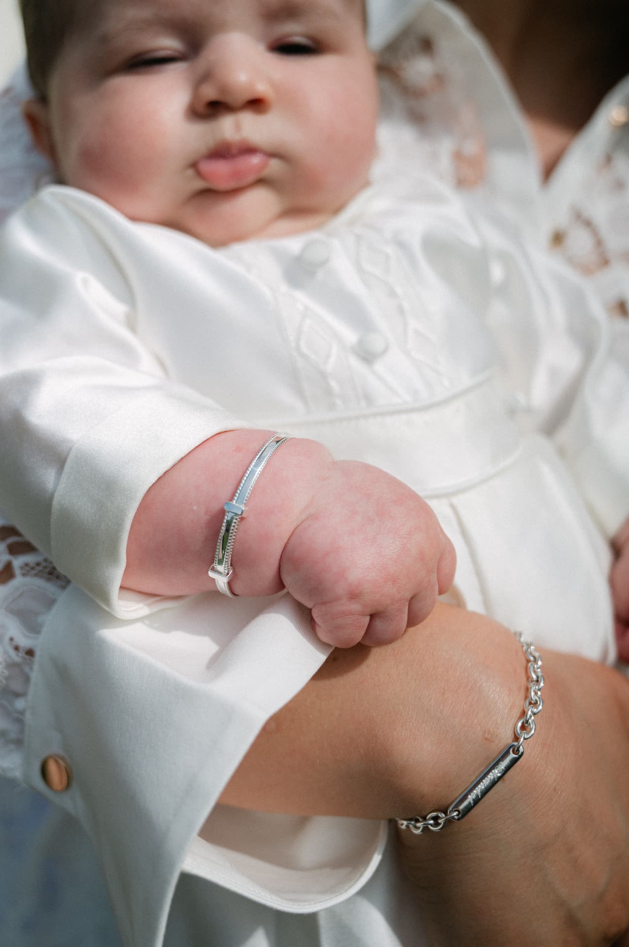 Close-up of a baby in a satin christening gown wearing a silver bangle