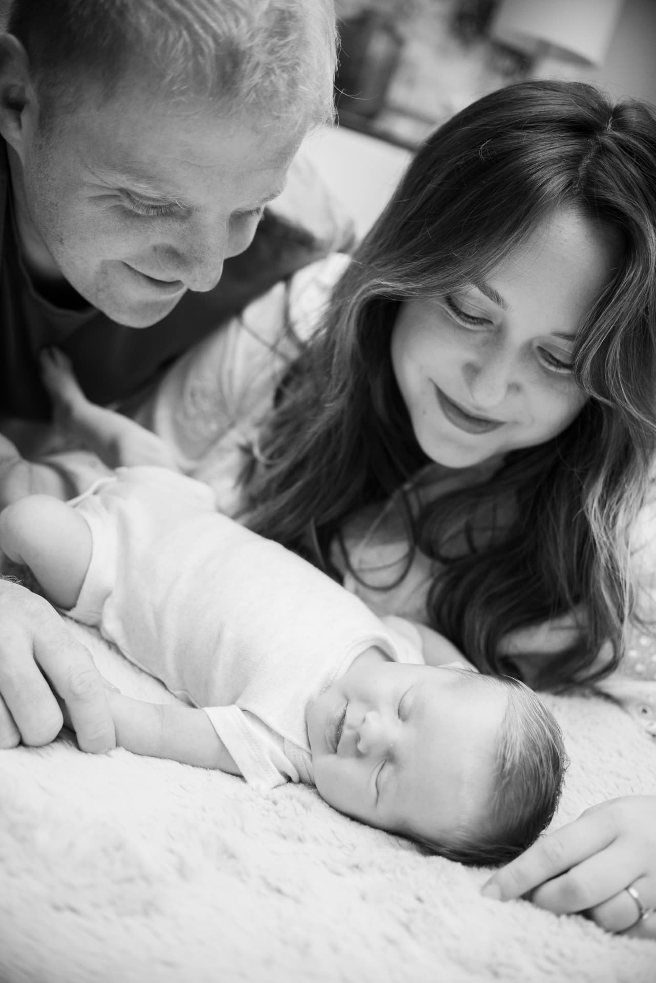 Black and white photograph of parents lying beside their sleeping newborn baby