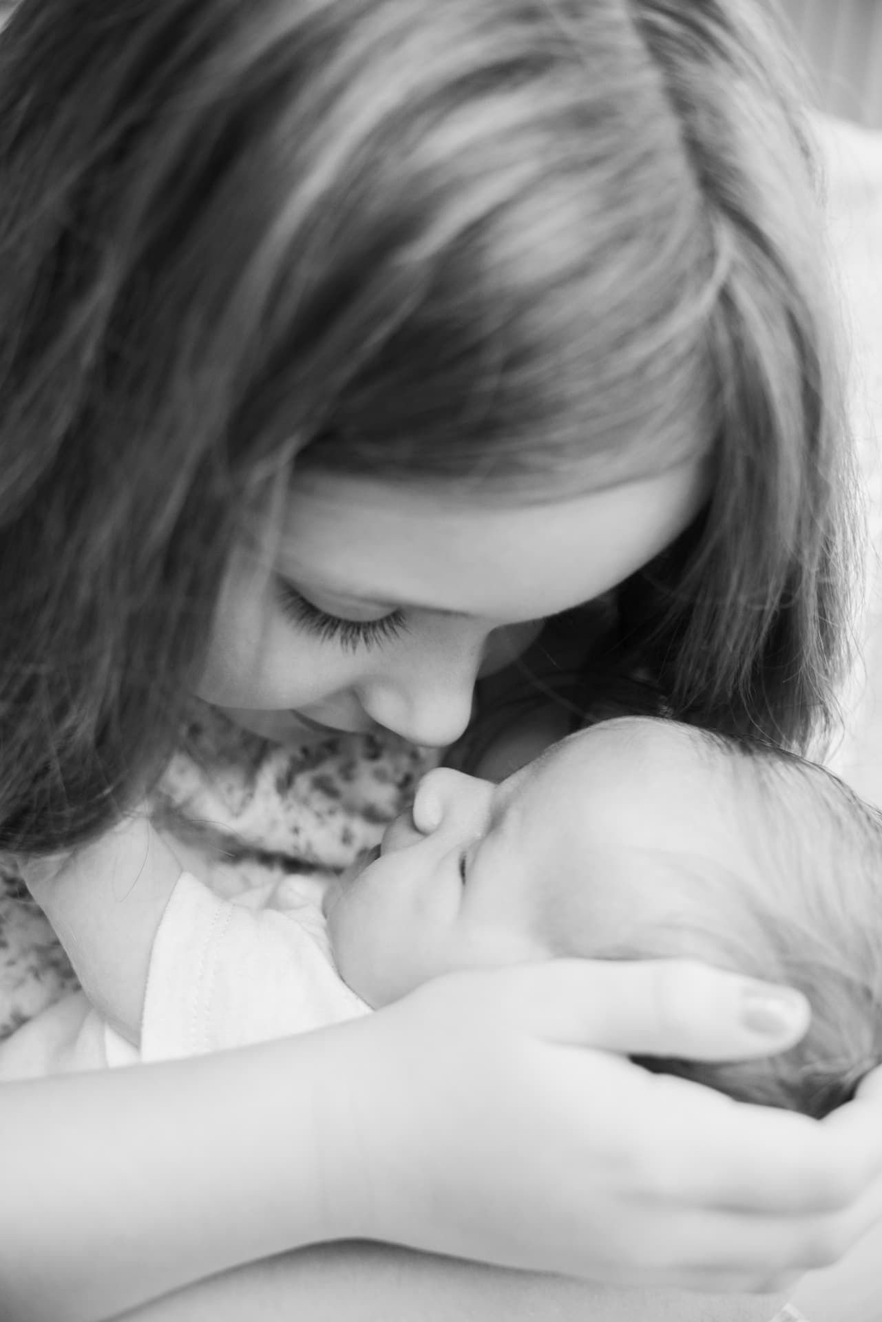 Black and white close-up of a sister gazing down tenderly at a newborn baby