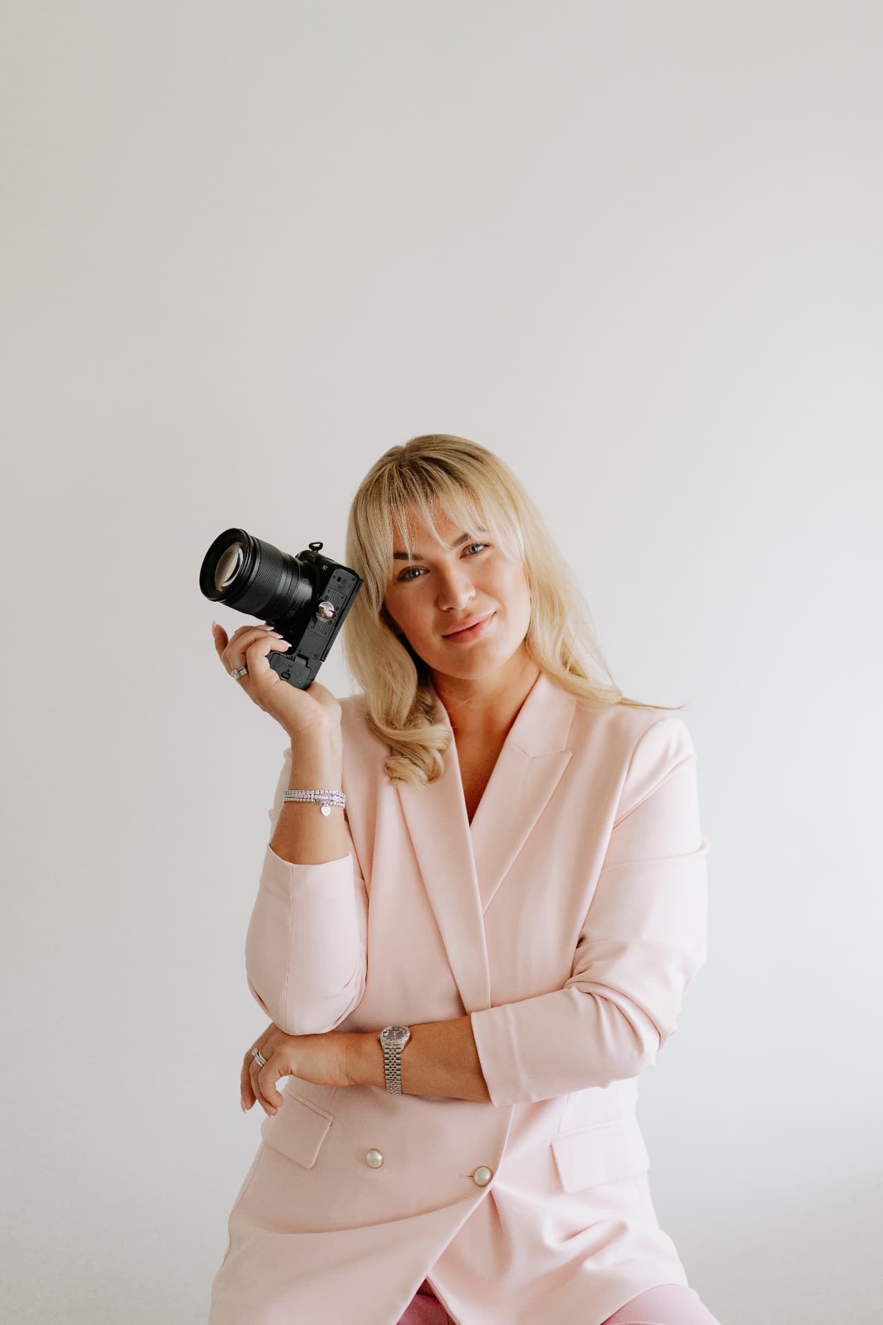 Robyn Francesca holding her camera over her shoulder in a pink suit
