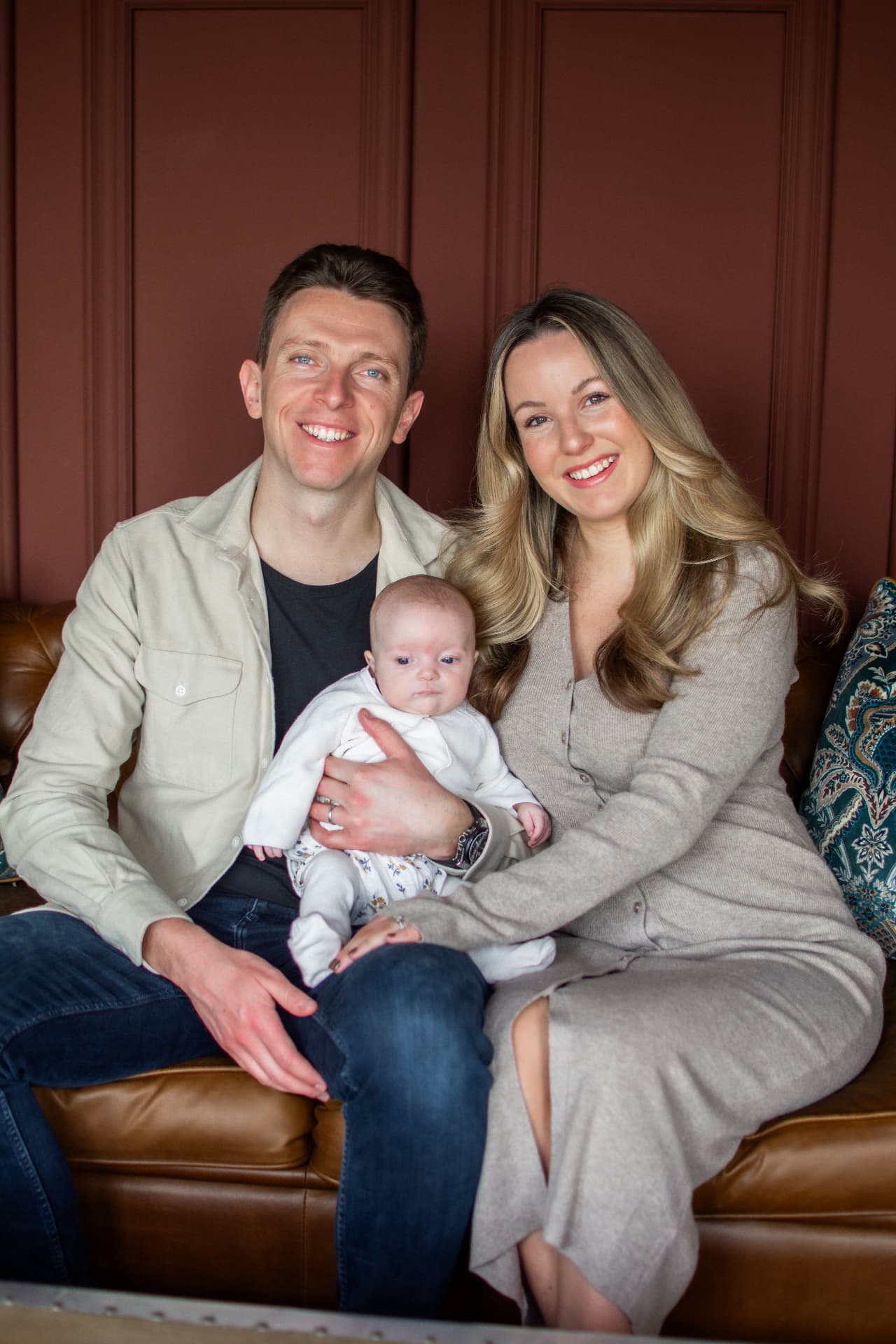 Parents sitting together on a sofa holding their baby at home