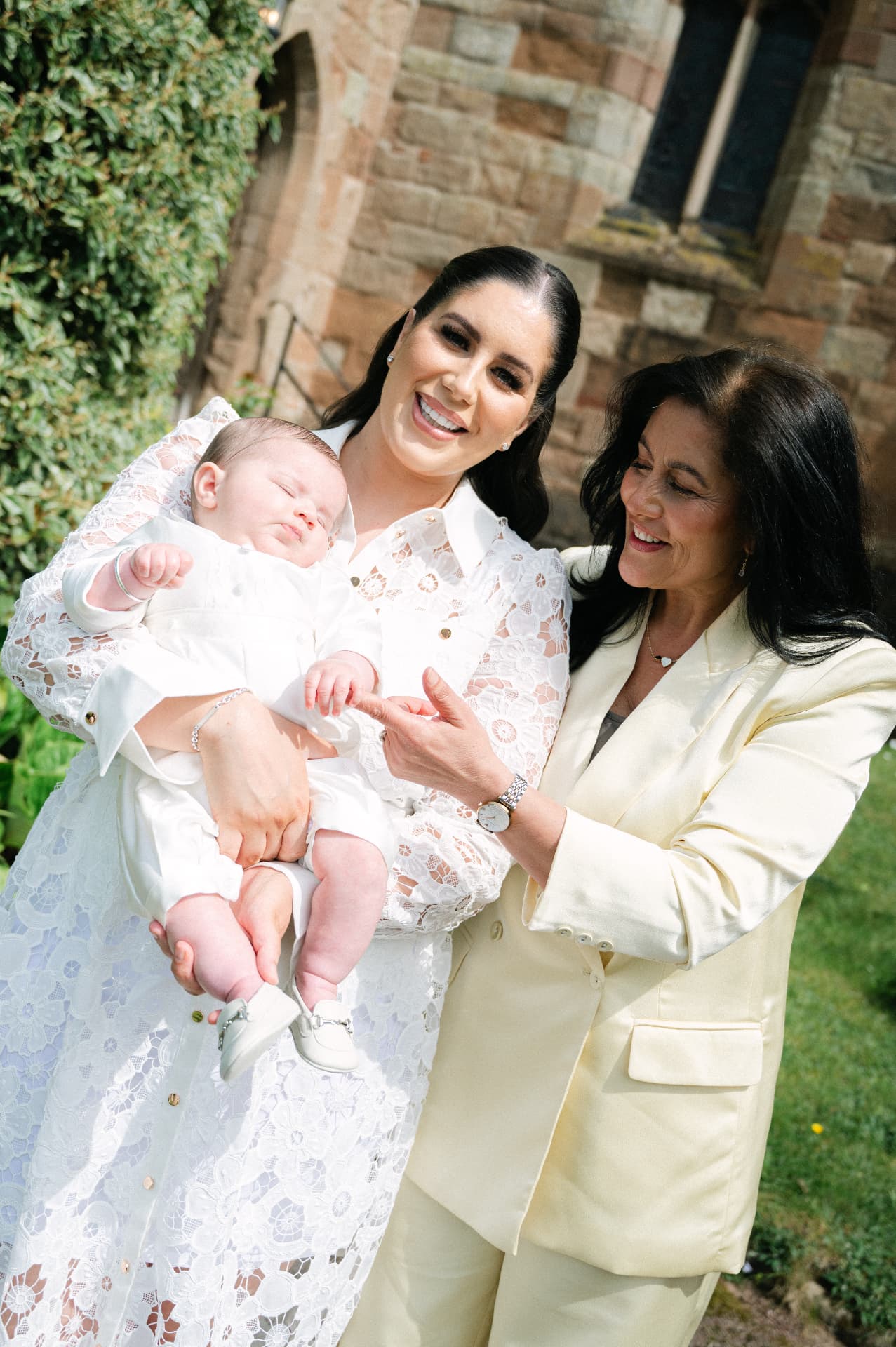 Mother and grandmother smiling with a baby outside a stone church