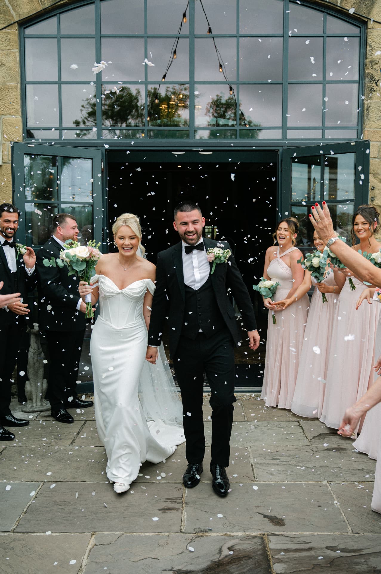 Bride and groom walking hand in hand through an arched doorway as confetti falls around them