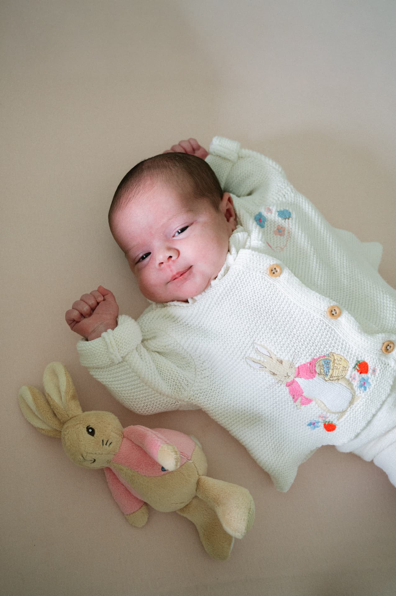 Newborn baby lying beside a Peter Rabbit soft toy in a knitted cardigan