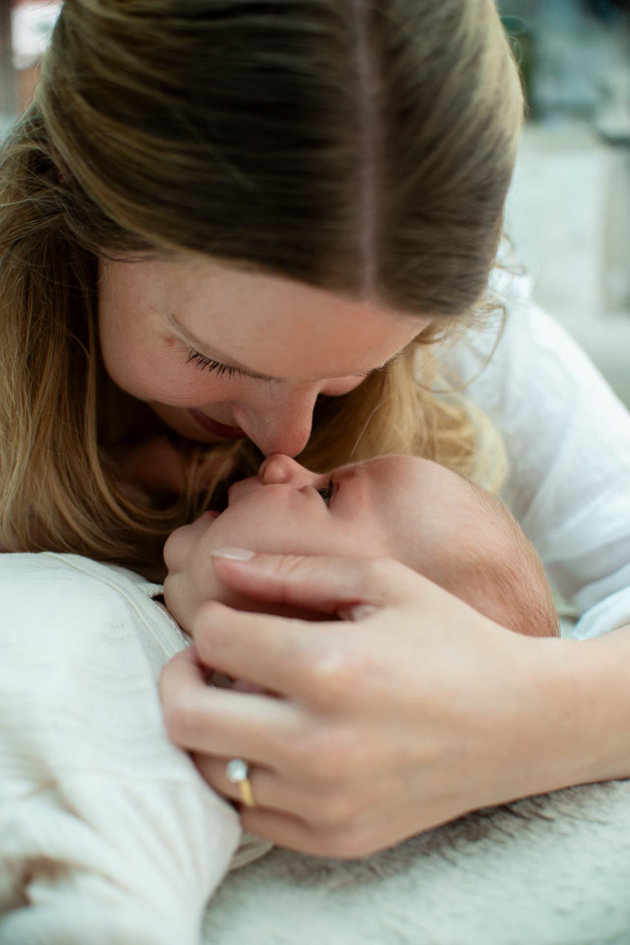 A mother kissing her baby's nose in soft natural light